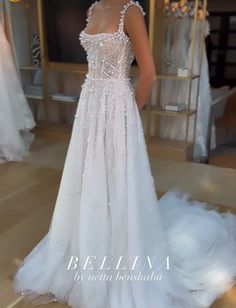 a woman standing in front of a dress on display at a bridal shop, wearing a white gown with sequins and beading