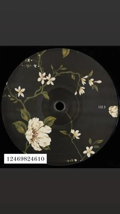 a black plate with white flowers and leaves painted on the side, in front of a black background