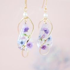 the earrings are decorated with purple flowers and glass beads on gold earwires that hang from hooks