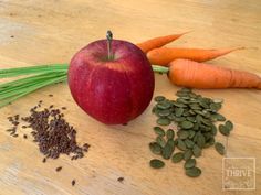 an apple, carrots and seeds on a wooden table