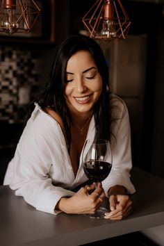 a woman sitting at a table with a glass of wine in her hand and smiling