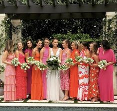 a group of women in dresses standing next to each other near a pool with greenery