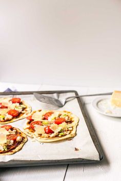 four small pizzas sitting on top of a metal tray next to a knife and fork