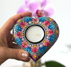 a hand holding a colorful heart shaped candle holder with a flower design on the inside