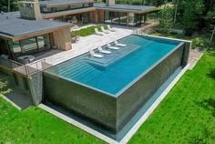 an aerial view of a house with a swimming pool in the foreground and lounge chairs on the lawn