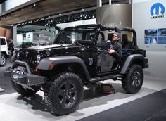 a man sitting in the driver's seat of a black jeep at an auto show