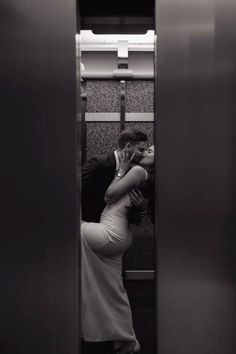 two people kissing in an elevator, one is on the phone and the other is standing up