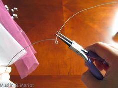 someone cutting wire with scissors on top of a wooden table next to pink and white napkins