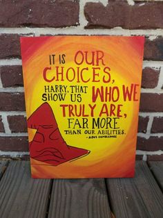 a painting on a wooden table with a brick wall in the background that says, it is our choices harry potters show us who we truly are far more than our abilities