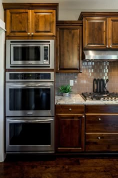 a kitchen with wooden cabinets and stainless steel appliances, including two ovens and one microwave