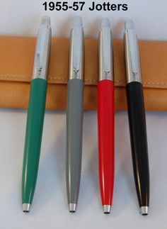 three different colored pens sitting next to each other on a white surface with leather case