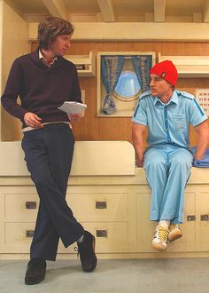 two men in scrubs are talking to each other while sitting on top of cabinets