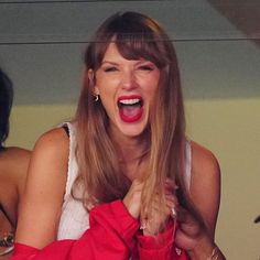 a woman holding onto a red jacket and smiling at the camera with her mouth open