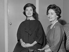 two women sitting next to each other in front of a door and one is holding a purse