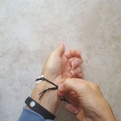 two hands holding onto each other with black string on their wrist and white dots on the wrist