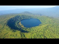 an aerial view of a lake in the middle of a forest with mountains in the background