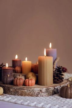 candles are arranged on a table with pine cones and pumpkins