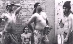 three men standing next to each other in front of a brick wall with graffiti on it