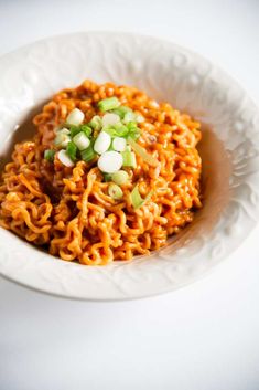 a white bowl filled with noodles topped with scallions and green onions on top