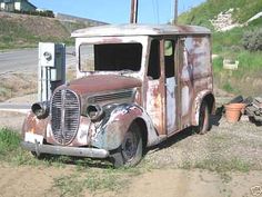 an old rusted out truck sitting on the side of a road