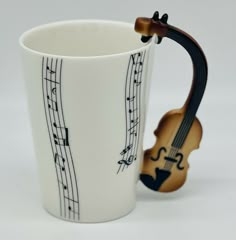 a coffee cup with musical notes on it and a violin in the middle, sitting next to it