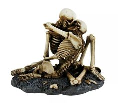 a figurine of a skeleton sitting on top of a rock with its head in his hands