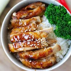 a white bowl filled with rice and meat covered in sesame seeds, broccoli