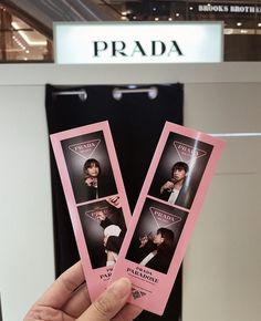 a person holding up two pink tickets in front of a prada sign