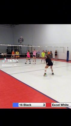 several girls are playing volleyball in an indoor court with red and white flooring, while one girl is about to hit the ball