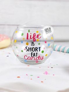 a glass bowl filled with confetti on top of a white table next to donuts