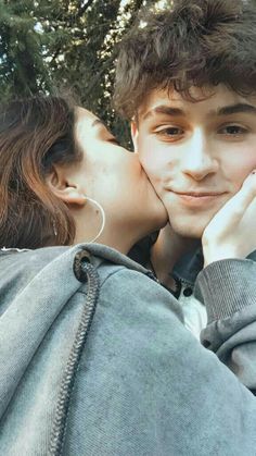 a young man and woman kissing each other in front of some trees with ear buds on their ears