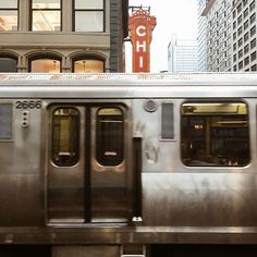 a silver train traveling down tracks next to tall buildings and a sign that reads chicago