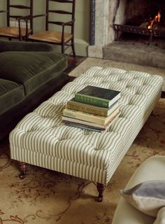 a stack of books sitting on top of a ottoman in front of a fire place