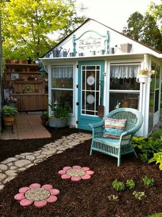 an image of a small garden shed with flowers on the ground and two chairs in front