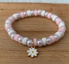 a close up of a bracelet on a wooden surface with a flower charm hanging from it