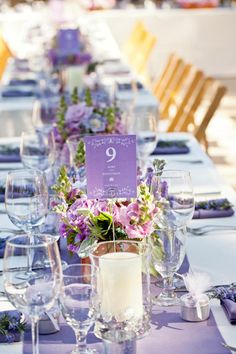 the table is set up with purple flowers and place settings for guests to sit at