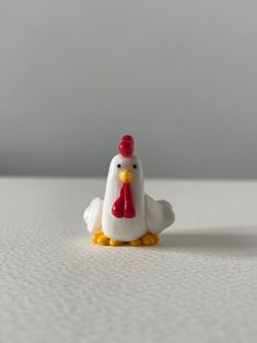 a small white chicken with a red hat on it's head sitting on a table