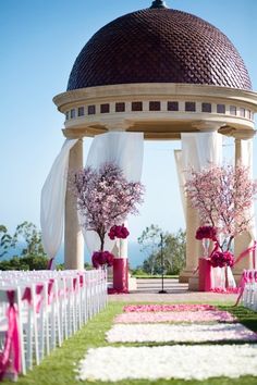 an outdoor wedding setup with pink flowers and white draping on the side of the aisle