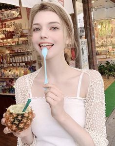 a woman holding a toothbrush in her mouth while standing next to a pineapple