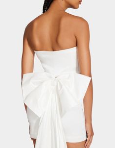 the back of a woman wearing a white dress with a large bow on her shoulder