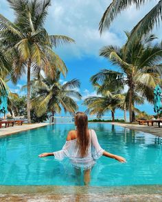 a woman sitting in the middle of a pool surrounded by palm trees