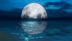 a full moon rising over the ocean with water reflecting it's reflection in the water