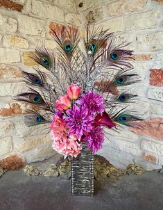 a vase filled with lots of purple flowers next to a brick wall and peacock feathers