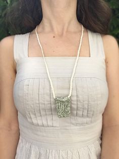 a woman wearing a white dress standing in front of some bushes with a necklace on her neck