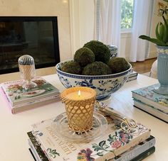 a table topped with books and a bowl filled with green moss covered balls next to a fire place