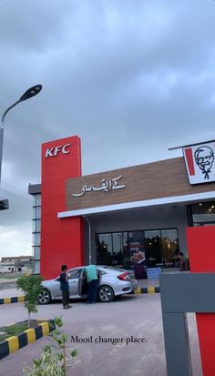 a car is parked in front of a kfc restaurant with two people standing outside