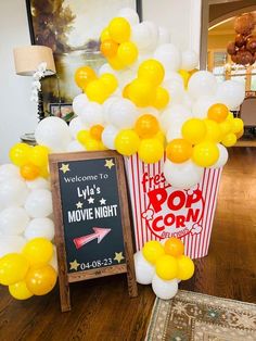 popcorn buckets filled with yellow and white balloons next to a chalkboard sign that says welcome to lyl's movie night