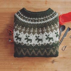 a knitted sweater sitting on top of a wooden table next to scissors and pliers