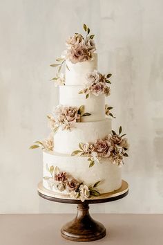 a three tiered wedding cake with pink flowers on the top and bottom, sitting on a wooden stand