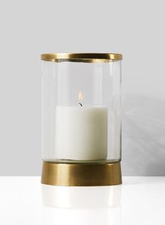 a white candle in a glass container with a gold rim and metal stand on a table